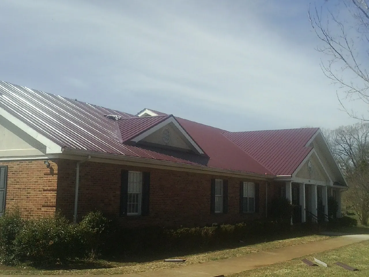Red metal roof with gabled entries on a long brick building, from a Hail Damage Roof Repair job in Swan Valley