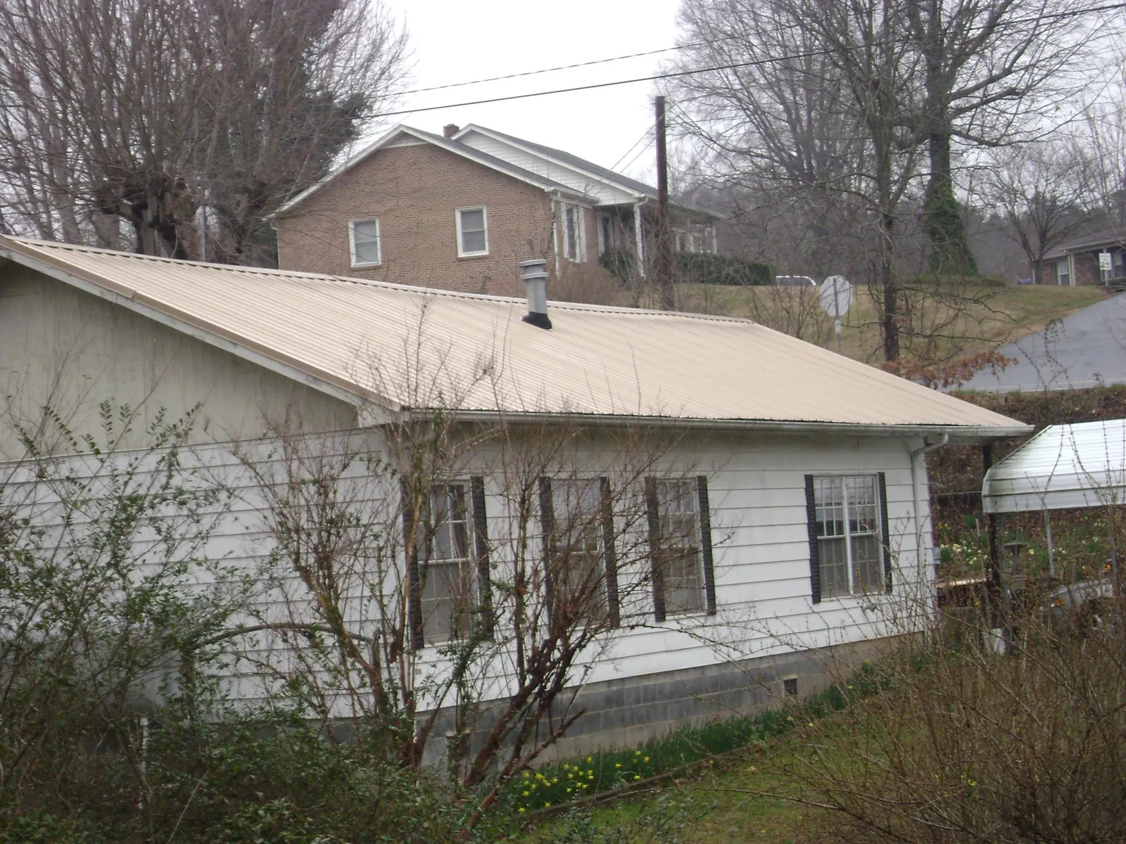 Tan metal roof on a white sided house set into a hillside — Commercial Roofing by Roofing Brothers in Swan Valley