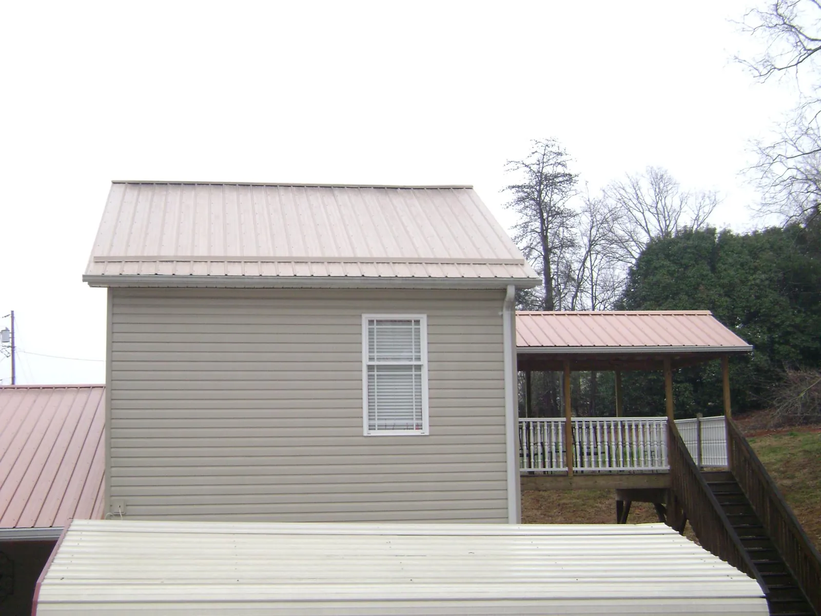 Tan metal roofs on a two story addition and attached porch, from a Roof Replacement job in Swan Valley